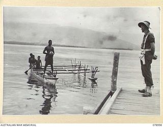 MALMAL VILLAGE, NEW BRITAIN. 1945-02-09. NATIVES IN A LAKATOI BRINGING A COCONUT INTO THE WHARF FOR A MEMBER OF THE 5TH DIVISION PROVOST COMPANY