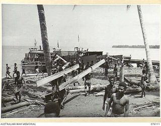 KARKAR ISLAND, NEW GUINEA. 1944-09-20. NATIVES WORKING UNDER THE DIRECTION OF THE AUSTRALIAN NEW GUINEA ADMINISTRATIVE UNIT LOADING TIMBER ON TO BARGES. THE TIMBER WILL BE USED IN RECONSTRUCTION ..