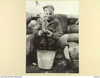 BOUGAINVILLE ISLAND, 1945-01-20. Q36779 PRIVATE J. MORRISON, 42ND INFANTRY BATTALION WASHING HIS CLOTHES IN A BUCKET OUTSIDE HIS COCONUT LOG DUGOUT