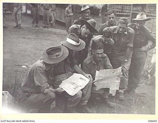 RABAUL, NEW BRITAIN. 1945-11-06. TROOPS OF HEADQUARTERS 11 DIVISION STUDYING THE RACING FORM FROM A NEWSPAPER BEFORE PLACING A BET ON THE MELBOURNE CUP