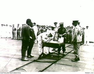 NEW BRITAIN, 1945-09-06. VICE ADMIRAL JINICHI KUSAKA, COMMANDER JAPANESE SOUTHEAST AREA FLEET, SIGNS THE INSTRUMENT OF SURRENDER ON BOARD HMS GLORY OFF RABAUL. (RNZAF OFFICIAL PHOTOGRAPH.)