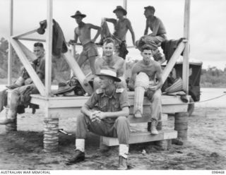 WEWAK AIRSTRIP, NEW GUINEA, 1945-10-30. MEMBERS OF 2/11TH INFANTRY BATTALION, WATCHING A CRICKET MATCH BETWEEN MEMBERS OF 30TH INFANTRY BATTALION, 8TH INFANTRY BRIGADE, USE A SALUTING BASE AS A ..