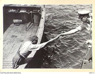 AT SEA, OFF BUIN, BOUGAINVILLE, 1945-08-20. LIEUTENANT-COMMANDER E. HOWITT, ROYAL AUSTRALIAN NAVY, HANDING A MESSAGE TO AN OFFICER ON A JAPANESE BARGE FOR RELAY TO LIEUTENANT-GENERAL M. KANDA, ..