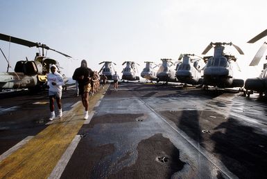 Crewmen and Marines run on the flight deck of the amphibious assault ship USS GUAM (LPH-9) during morning physical training (PT)