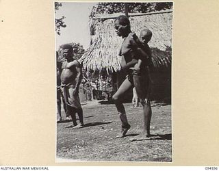 SIPILANGAN, NEW BRITAIN, 1945-07-27. A REFUGEE NATIVE WOMAN CARRYING A PICCANINNY AT THE AUSTRALIAN NEW GUINEA ADMINISTRATIVE UNIT REFUGEE CAMP, WIDE BAY AREA. AT PRESENT THE CAMP HOUSES ..