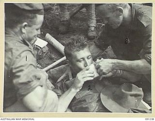 BOUGAINVILLE. 1945-04-26. BATTLE CASUALTY TPR C. PARKER, 2/4 ARMOURED REGIMENT (2), HAVING A DRINK OF TEA AT B COMPANY, 24 INFANTRY BATTALION. HE WAS SHOT THROUGH THE LEG DURING 24 INFANTRY ..