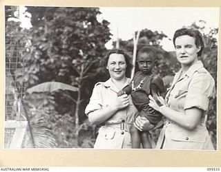 WUNUNG, JACQUINOT BAY, NEW BRITAIN, 1945-08-25. PRIVATE I. BENTON (1) AND PRIVATE M. KENT (2) AUSTRALIAN ARMY MEDICAL WOMEN'S SERVICE MEMBERS OF 2/8 GENERAL HOSPITAL, WITH LUSI, A CHILD AT THE ..