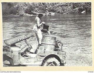 BOUGAINVILLE ISLAND. 1945-03-08. Q103459 PRIVATE J.K. HEALY, A COMPANY, 25TH INFANTRY BATTALION FILLING A 44 GALLON DRUM WITH DRINKING WATER FROM THE PURIATA RIVER