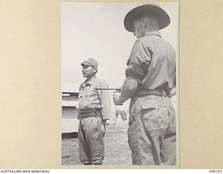 CAPE WOM, NEW GUINEA. 1945-10-19. CORPORAL YAMAMOTO, OF THE JAPANESE ARMY (1), BEING GUARDED BY CORPORAL A.J. HOBBS, HEADQUARTERS 6 DIVISION PROVOST CORPS (2), WHILE WAITING TO BE QUESTIONED BY THE ..