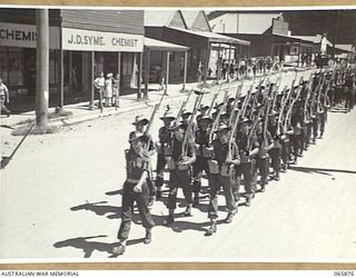HERBERTON, QLD. 1944-04-25. THE SECOND PLATOON OF THE REPRESENTATIVE COMPANY OF PERSONNEL OF THE 6TH DIVISION AT J. D. SYME, CHEMIST, MARCHING ALONG THE MAIN STREET TO THE WAR MEMORIAL TO TAKE PART ..