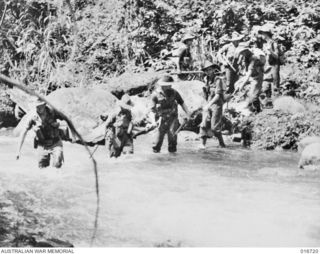 1944-03-23. NEW GUINEA. MEMBERS OF THE AUSTRALIAN JUNGLE PATROL FEATURED IN THE DEPARTMENT OF INFORMATION FILM "JUNGLE PATROL" FORM A NATURAL CHAIN LINKING THEIR RIFLES TO CROSS FAST RUNNING FARIA ..