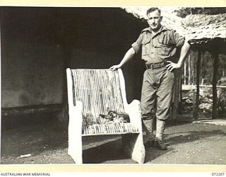 NEW GUINEA. 1944-04-04. NX155619 SIGNALMAN L.S. RALPH, 23RD LINE SECTION, 18TH LINES OF COMMUNICATION SIGNALS ALONGSIDE A CHAIR CONSTRUCTED BY HIM FROM BAMBOO AND SECTIONS OF AN IRONWOOD TREE