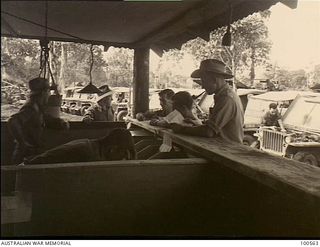 Lae, New Guinea. 1944-06-30. Captain R. Adamson, Officer in Charge, Transport Section, HQ, New Guinea Force, in his office. Note the line up of jeeps that are all prepared for immediate despatch
