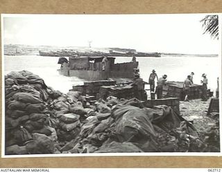 SIALUM, NEW GUINEA. 1944-01-05. STACKS OF MAIL FOR PERSONNEL OF THE 9TH AUSTRALIAN DIVISION ON THE BEACH. SUPPLY BARGES CAN BE SEEN MOORED ON SIALUM ISLAND IN THE BACKGROUND