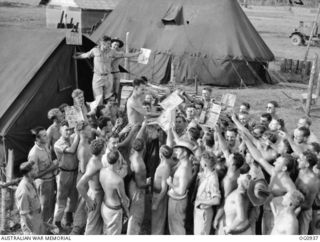 NADZAB, NEW GUINEA. C. 1944-02. DIVE BOMBER BOYS CROWD AT THE POST OFFICE WHEN A NEW BUNDLE OF PHOTOS ARRIVE AT NO. 24 (VENGEANCE) SQUADRON RAAF FROM THE "ADOPTED" TIVOLI GIRL PERFORMERS. THE ..