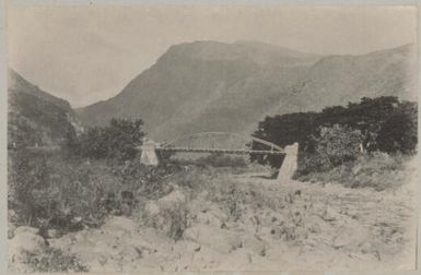 Bridge over a rocky river bed with a mountain in the background on an island in the Pacific Ocean, approximately 1895