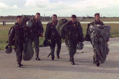 Straight on medium shot of US Marines from Company A, 5th Reconnaissance Battalion, 3rd Marine Division, walk together as a team across the tarmac after jumping from a US Air Force C-141 Starlifter (Not Shown) and landing successfully with their MC5 parachutes during Force Reconnaissance Exercises at Andersen Air Force Base, Guam. From left to right are; Gunny Sergeant Longnecker, STAFF Sergeant Pitchford, Corporal Foran, Lance Corporal Arguemedo and Corporal Anson