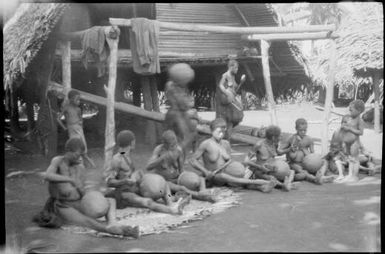 Seven women seated on mats while working on pots with two women standing behind, Madang, New Guinea, ca. 1935 / Sarah Chinnery