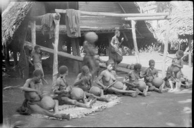 Seven women seated on mats while working on pots with two women standing behind, Madang, New Guinea, ca. 1935 / Sarah Chinnery