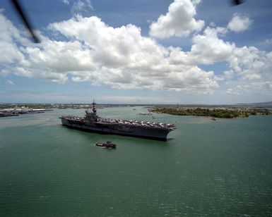 Sailors man the rails aboard the aircraft carrier USS RANGER (CV-61) as the vessel approaches the Naval Supply Center pier for docking. The carrier is being assisted by the large harbor tugs TUSKEGEE (YTB-806) and WAXAHATCHIE (YTB-814). The RANGER is stopping off at Pearl Harbor while en route to its home port after returning from deployment in the Persian Gulf during Operation Desert Storm