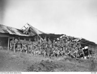 WAREO, NEW GUINEA. 1943-12-09. SOME OF THE OFFICERS AND MEN OF D COMPANY, 2/23RD AUSTRALIAN INFANTRY BATTALION IN FRONT OF A BOMB DAMAGED COWSHED. THE JAPANESE, DURING THEIR OCCUPATION OF THE AREA ..