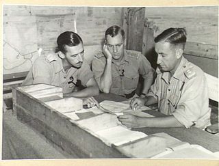 Group portrait of the Commanding Officer of the 18th Field Ambulance holding a conference in his tent with his second in charge and the Duty Medical Officer. Identified from left to right: NX113200 ..