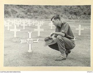 SALAMAUA, NEW GUINEA. 1944-10-01. VX61309 SERGEANT M.A. BARR, NEW GUINEA PRESS UNIT, EXAMINING THE GRAVE OF HIS BROTHER IN THE AUSTRALIAN WAR CEMETERY (VX39195 CAPTAIN F.A. BARR, 2/7TH INFANTRY ..