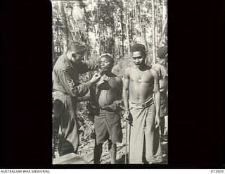 SHAGGY RIDGE, RAMU VALLEY, NEW GUINEA. 1944-06-18. VX128013 SERGEANT G. J. BROWNING PUTTING WAR PAINT ON A NATIVE CARRIER BOY AT SHAGGY RIDGE. A PATROL FROM 11TH DIVISION CARRIER COMPANY IS ..