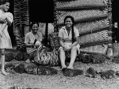 [Portrait of women holding coconuts in front of dwelling]