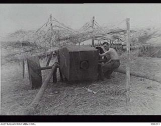 GOODENOUGH ISLAND, NEW GUINEA, 1942-10. AN AUSTRALIAN SOLDIER SETTING IN POSITION A DEFENCE GUN MADE OF LOGS. THIS WAS PART OF A MASTERPIECE OF BLUFF AND DECEPTION, BY WHICH THE SMALL GROUP OF ..