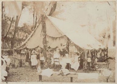 Reverend and Mrs Hutchin, Ariki Makea Takau and others seated under an awning at a garden party. From the album: Cook Islands