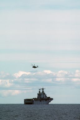 A starboard quarter view of the amphibious assault ship USS SAIPAN (LHA 2) with a CH-53E Super Stallion helicopter overhead during NATO Exercise NORTHERN WEDDING 86