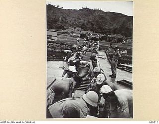 RABAUL, NEW BRITAIN. 1945-11-03. JAPANESE TROOPS, WATCHED BY A MEMBER OF 33 PORT OPERATING COMPANY, UNLOAD STORES AT THE BP WHARF. ROLLERS ARE USED TO TRANSFER THE GOODS FROM SHIP TO TRUCK