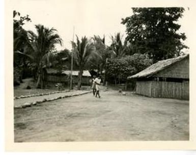 [Two Melanesian Individuals Walking in a Guadalcanal Village]