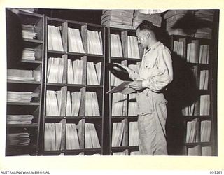 JACQUINOT BAY, NEW BRITAIN, 1945-08-12. SERGEANT G.A.A. ELLIS, SELECTING A RECORD IN THE RECORD LIBRARY OF THE NEW RADIO STATION 9AE OPERATED BY AUSTRALIAN ARMY AMENITIES SERVICE