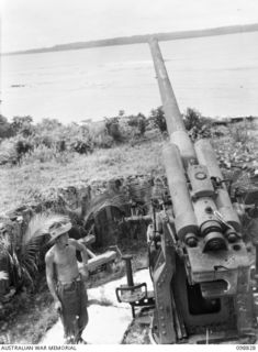 BALLALAE ISLAND, BOUGAINVILLE AREA. 1945-11-10. A MEMBER OF 7 INFANTRY BATTALION EXAMINING ONE OF THE MANY HEAVY ANTI-AIRCRAFT GUNS WHICH HELPED TO PROTECT THE AIRSTRIP. THE GUN IS STILL IN GOOD ..