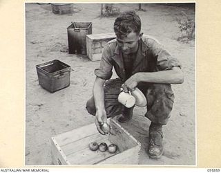BORAM, WEWAK AREA, NEW GUINEA. 1945-08-31. LANCE CORPORAL J.D. GREGORY, 2/41 LIGHT AID DETACHMENT, CORPS OF AUSTRALIAN ELECTRICAL AND MECHANICAL ENGINEERS, TAKING AN APPLE FROM THE BOX OUTSIDE THE ..