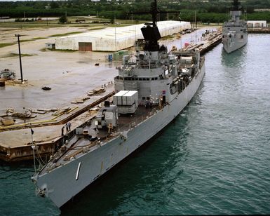 A port bow view of the guided missile frigate USS BROOKE (FFG 1), front, and the frigate USS BADGER (FF 1071) moored at a pier