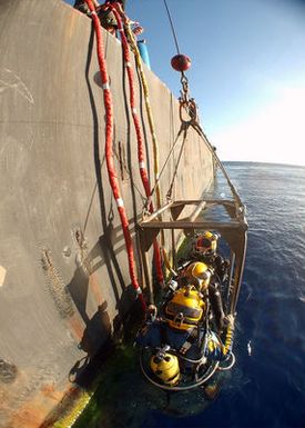 US Navy (USN) divers assigned to Mobile Diving and Salvage Unit One (MDSU-1) and Japanese Self Defense Force divers, are lowered into the waters off the coast of Hawaii, by crewmembers aboard the Crowley 450-10 barge, during recovery operations for the Japanese fishing vessel Ehime Maru