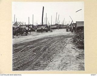 WIRUI BEACH, WEWAK AREA, NEW GUINEA. 1945-08-31. THE APPROACH TO THE MAIN DRESSING STATION RECEPTION ROOM, 2/1 FIELD AMBULANCE SHOWING THE MAIN DRESSING STATION SIGN. A SIMILAR CIRCULAR SIGN STANDS ..