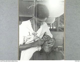 LAE, NEW GUINEA. 1944-09-18. NX76594 MAJOR H. THOMPSON, DENTAL OFFICER, ATTENDING TO A PATIENT IN HIS SURGERY AT HEADQUARTERS NEW GUINEA FORCE