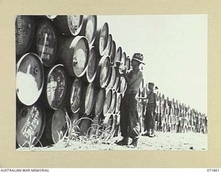 LAE, NEW GUINEA. 1944-03-30. TX1019 PRIVATE C. HILL (FOREGROUND), AND T30174 PRIVATE K. J. EVERETT (BACKGROUND), MEMBERS OF THE 55TH BULK ISSUE PETROL AND OIL DEPOT PLATOON, TIGHTEN THE BUNGS ON ..