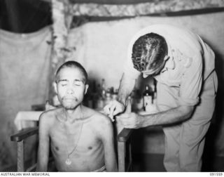 SORAKEN AREA, BOUGAINVILLE. 1945-04-03. CAPTAIN C.H. WOOD, 19 FIELD AMBULANCE, GIVING TREATMENT TO ONE OF THE AMBOINESE ESCAPEES AT THE REGIMENTAL AID POST