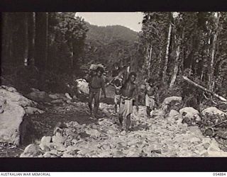 BULLDOG-WAU ROAD, NEW GUINEA, 1943-07-12. NATIVE CARRIERS WALKING ALONG A PARTLY MADE SECTION OF ROAD AT THE 13 MILE POINT