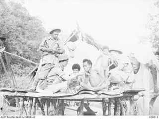 PAPUA, NEW GUINEA. 1942. DIGGERS OF B COMPANY 55/53RD BATTALION AIF, HAVE A SMOKE WITH A NATIVE FAMILY ON THEIR VERANDAH, AS THEY PASS THROUGH THE VILLAGE DURING A PATROL. SHOWN: PRIVATE L. SCALON ..