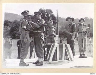 TOROKINA, BOUGAINVILLE. 1945-09-24. MAJOR GENERAL W. BRIDGEFORD, GENERAL OFFICER COMMANDING 3 DIVISION, PRESENTING CAPTAIN E.M. GRIFF WITH THE MILITARY CROSS DURING PRESENTATION OF AWARDS AND MARCH ..