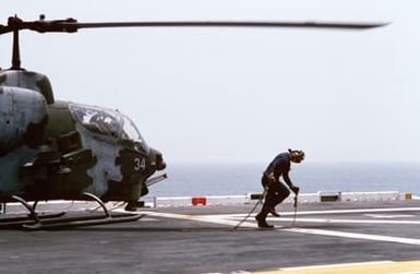 Flight deck crewman aboard the amphibious assault ship USS SAIPAN (LHA 2) carry tie-down chains away from an AH-1J Sea Cobra helicopter attached to Marine Medium Helicopter Squadron 261 (HMM-261) as flight operations are conducted during Operation Sharp Edge. Marines embarked aboard the SAIPAN have been sent the U.S. Embassy in Monrovia, Liberia, to augment security and evacuate U.S. and foreign nationals from the fighting between government and rebel forces