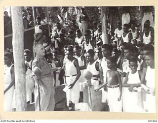 TOROKINA, BOUGAINVILLE. 1945-10-03. FATHER R.P. O'SULLIVAN CONDUCTS THE NATIVE CHOIR DURING THE SOLEMN HIGH MASS OF THANKSGIVING FOR PEACE HELD AT GLOUCESTER PARK OVAL AND ATTENDED BY MEMBERS OF ..