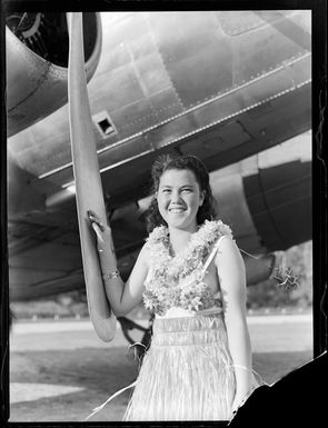 Unidentified local girl wearing a hula skirt beside a C47 transport aircraft, Rarotonga airfield, Cook Islands