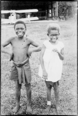 Two children with a bi-plane in the background, New Guinea, ca. 1935 / Sarah Chinnery